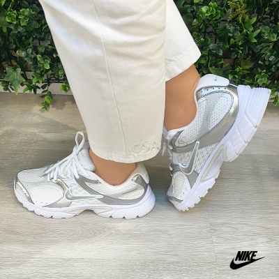 Ténis Nike brancos e prateados usados por uma pessoa com calças claras
