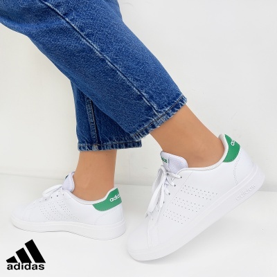 Ténis Adidas brancos com detalhes verdes usados com calças de ganga azuis