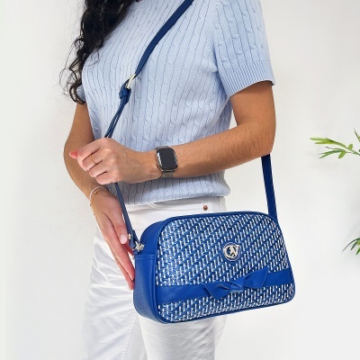 Mala de ombro azul com padrão entrelaçado branco e azul e aplique de fita decorativa azul, mulher com roupa azul clara e branca