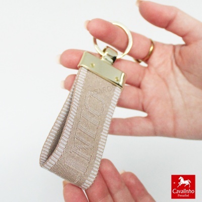 Chaveiro tecido bege com acabamento metálico dourado e marca Cavalinho