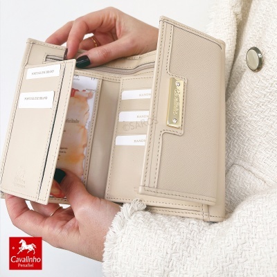 Carteira bege de pele com fecho dourado e vários compartimentos aberta nas mãos