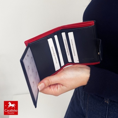 Carteira azul e vermelha de couro aberta com cartões HANDMADE IN PORTUGAL, segurada por mão com fundo escuro