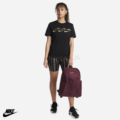 Mulher com t-shirt preta e calções com padrão dourado, mochila bordeaux e ténis pretos de fundo branco