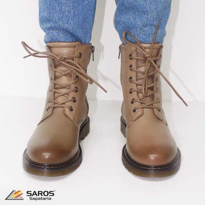 Botas castanho claro em pele com atacadores e sola preta, usadas com calças de ganga azuis sobre fundo branco.