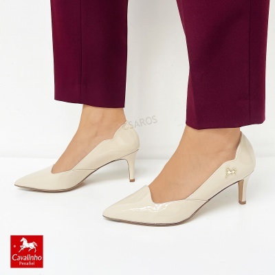 Sapatos de salto alto em verniz bege com detalhe dourado, em fundo branco.