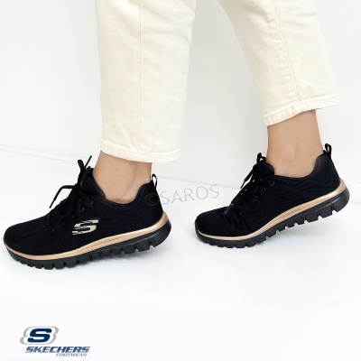 Ténis pretos Skechers com sola preta e dourada usados por pessoa