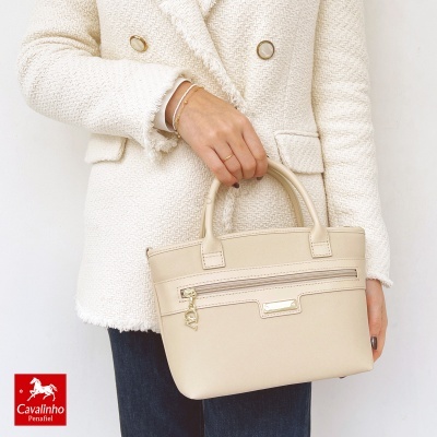 Mala de mão bege com fecho e pendente dourado, casaco branco texturizado, fundo branco.