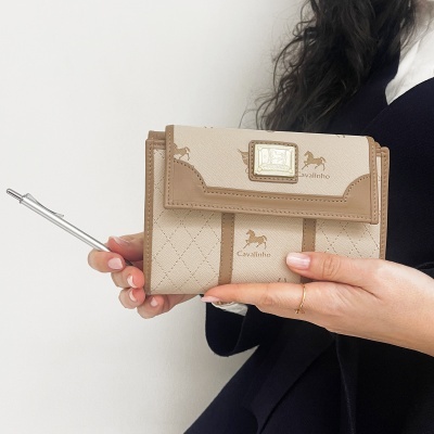 Carteira bege e castanha Cavalinho com padrão de cavalos e relevo, segurada por pessoa em fundo branco.