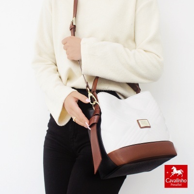 Mala de ombro branco com base castanha e detalhes pretos, usada por mulher com camisola branca e calças pretas