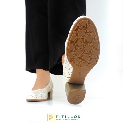 Sapatos de salto médio perfurados brancos com sola castanha, calças pretas, fundo branco com logótipo Pitillos.