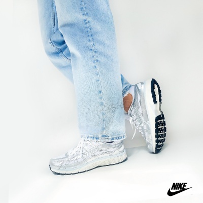 Ténis desportivos Nike prateados com sola preta usados com calças de ganga azuis claras