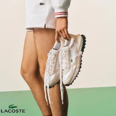 Pessoa segurando sapatilhas brancas Lacoste com detalhes bege e sola preta.