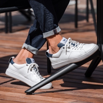 Ténis brancos de pele com detalhes azuis usados por pessoa sentado numa cadeira preta.