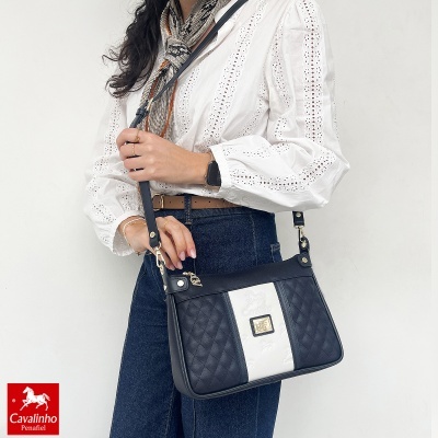Mala preta e branca Cavalinho matelassê com detalhes dourados usada por mulher com blusa branca e jeans