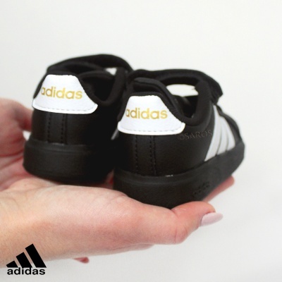 Tênis infantis Adidas em couro preto com detalhes brancos e logo Adidas amarelo.
