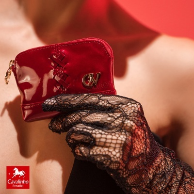 Carteira pequena vermelha brilhante com detalhes dourados e mão com luva preta rendada