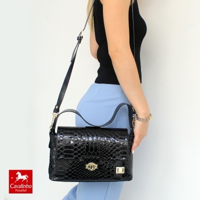 Mala preta com textura imitação pele de crocodilo, alça tiracolo, mulher a segurá-la