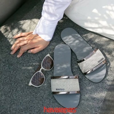 Sandálias cinzentas Havaianas e óculos de sol brancos sobre chão cinzento