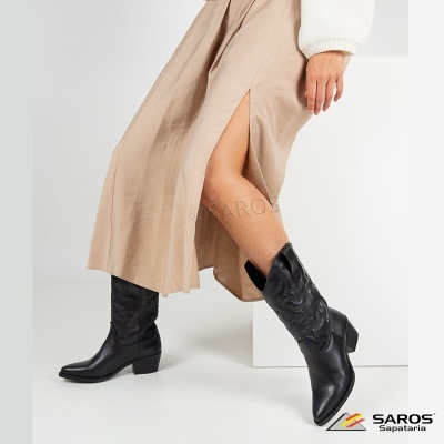 Botas pretas estilo cowboy em pele com padrão decorativo usadas com saia bege