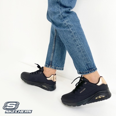 Ténis Skechers pretos com detalhes dourados usados com jeans azuis