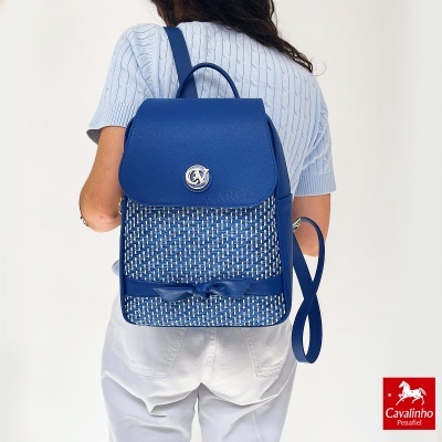 Mochila azul com padrão entrelaçado branco e azul, com fecho metálico e laço, usada por mulher