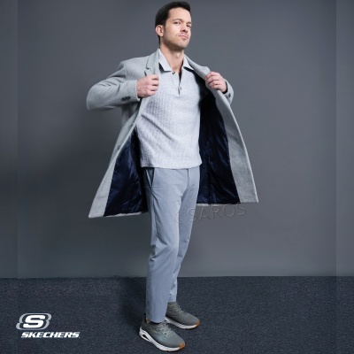 Homem vestido casual com casaco cinza, polo branco e ténis Skechers cinza