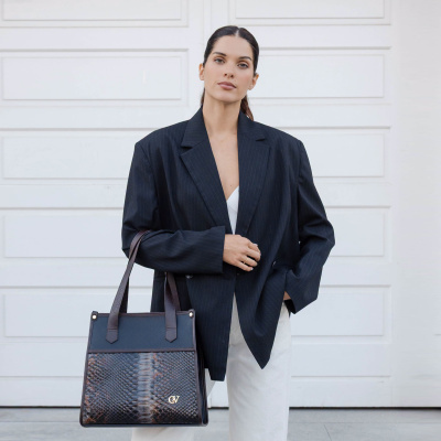 Mulher com blazer preto e mala preta com padrão de pele de cobra em fundo branco
