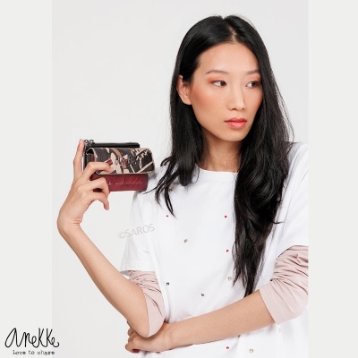 Carteira pequena animal print castanho e bege com detalhe bordô na mão de mulher com cabelo preto e t-shirt branca