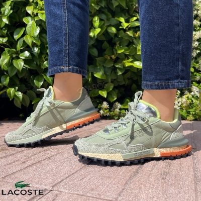 Tênis verdes Lacoste com sola preta, creme e laranja, em chão de tijoleira ao ar livre
