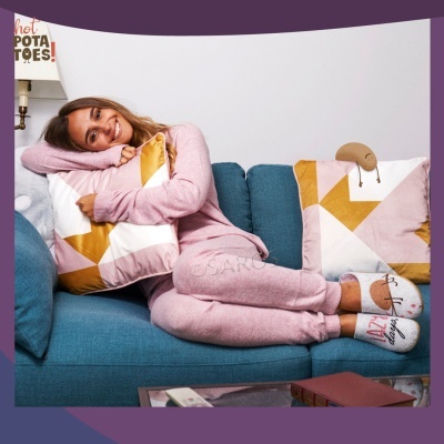 Mulher em pijama rosa e meias cinza deitada e abraçando almofada geométrica no sofá azul