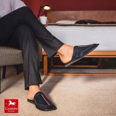 Sapatos mule pretos com faixa tricolor sobre tapete bege num quarto