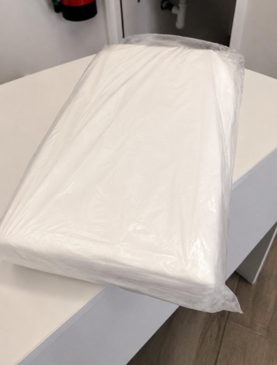 Pacote retangular com objeto branco envolto em plástico transparente numa mesa branca