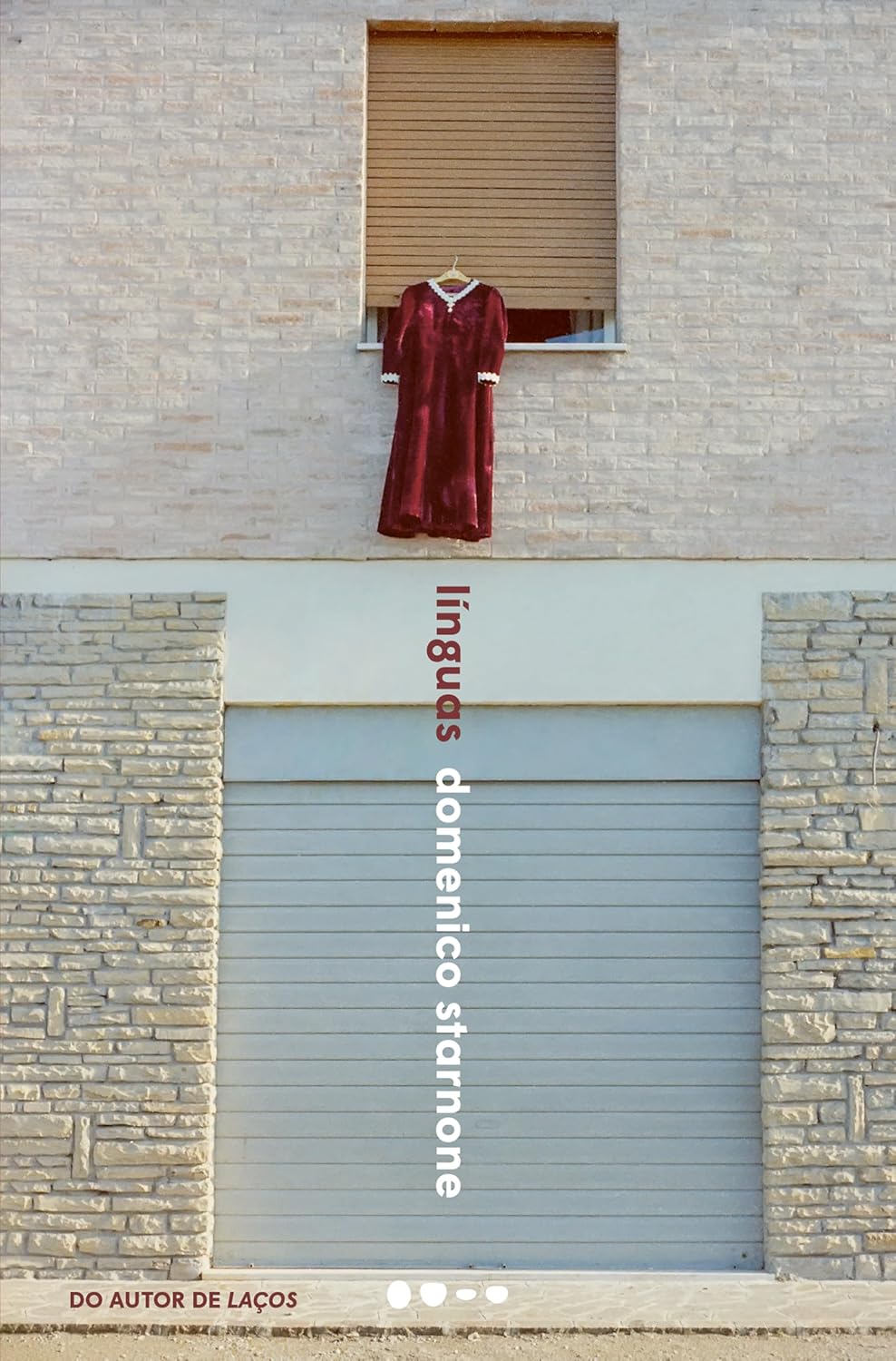Línguas Vestido de veludo bordô com detalhes brancos pendurado numa janela de estore castanho numa parede de tijolos claros com texto vertical e rodapé.