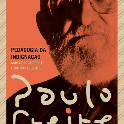 Capa de livro Pedagogia da Indignação com rosto de homem idoso com barba e óculos em fundo laranja.
