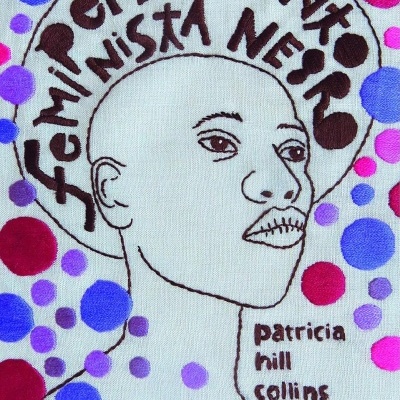 Bordado com rosto humano e texto FEMINISMO NEGRO, patricia hill collins, em tecido com pontos coloridos.