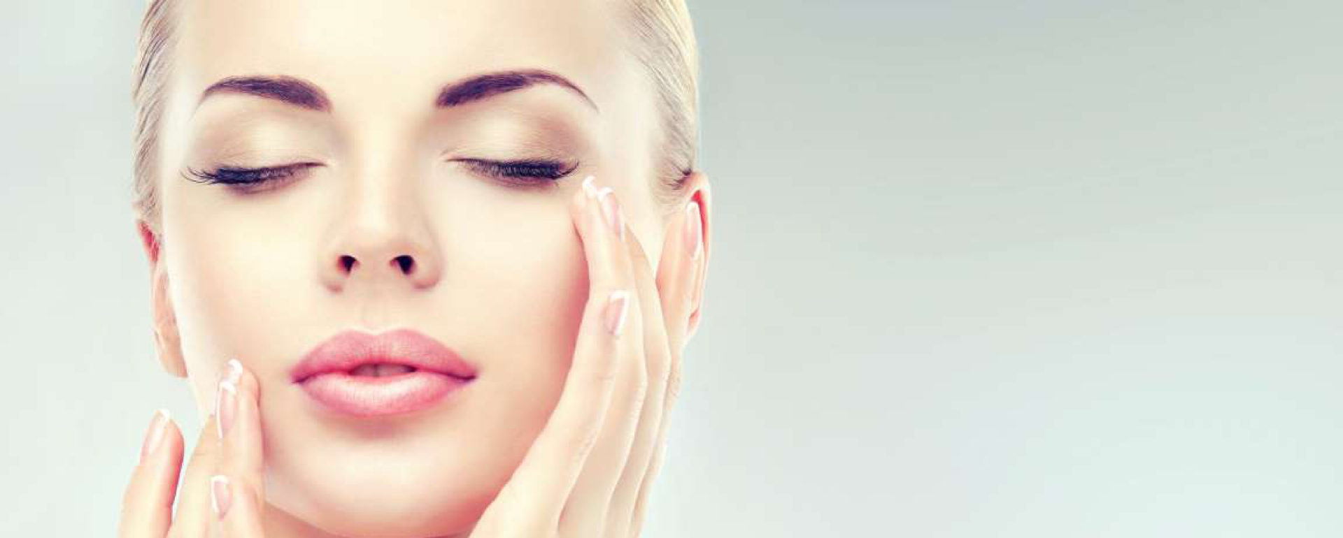 Mulher loira com olhos fechados tocando rosto com mãos, fundo cinza claro.