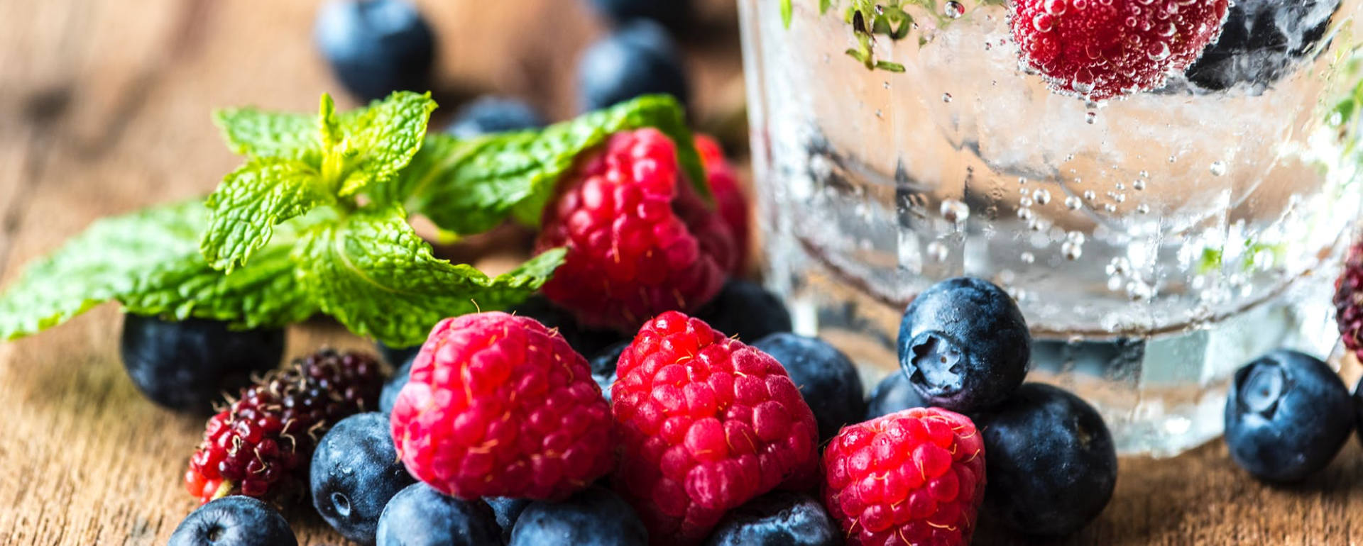 Frutas vermelhas frescas sobre madeira com hortelã e copo com líquido