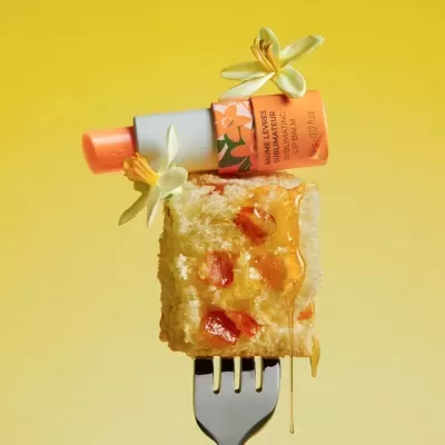 Bálsamo labial sobre bolo com mel e duas flores, fundo amarelo