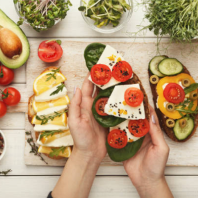 Três torradas variadas com legumes frescos e queijo sobre tabuleiro de madeira