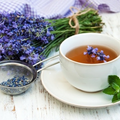 Xícara branca de chá com infusão de flores violetas e ramo de lavanda