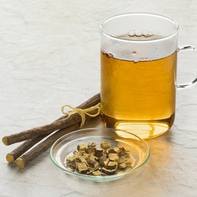 Copo transparente com bebida âmbar, paus castanhos amarrados e prato com pedaços de madeira sobre mesa clara