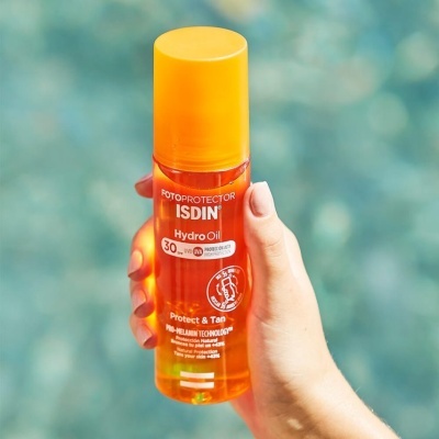 Frasco de óleo fotoprotetor ISDIN Hydro Oil SPF 30 com tampa amarela na mão