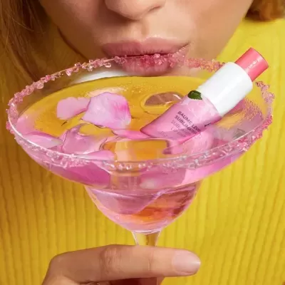 Bálsamo labial rosa em copo de cocktail com pétalas de rosa e açúcar rosa na borda