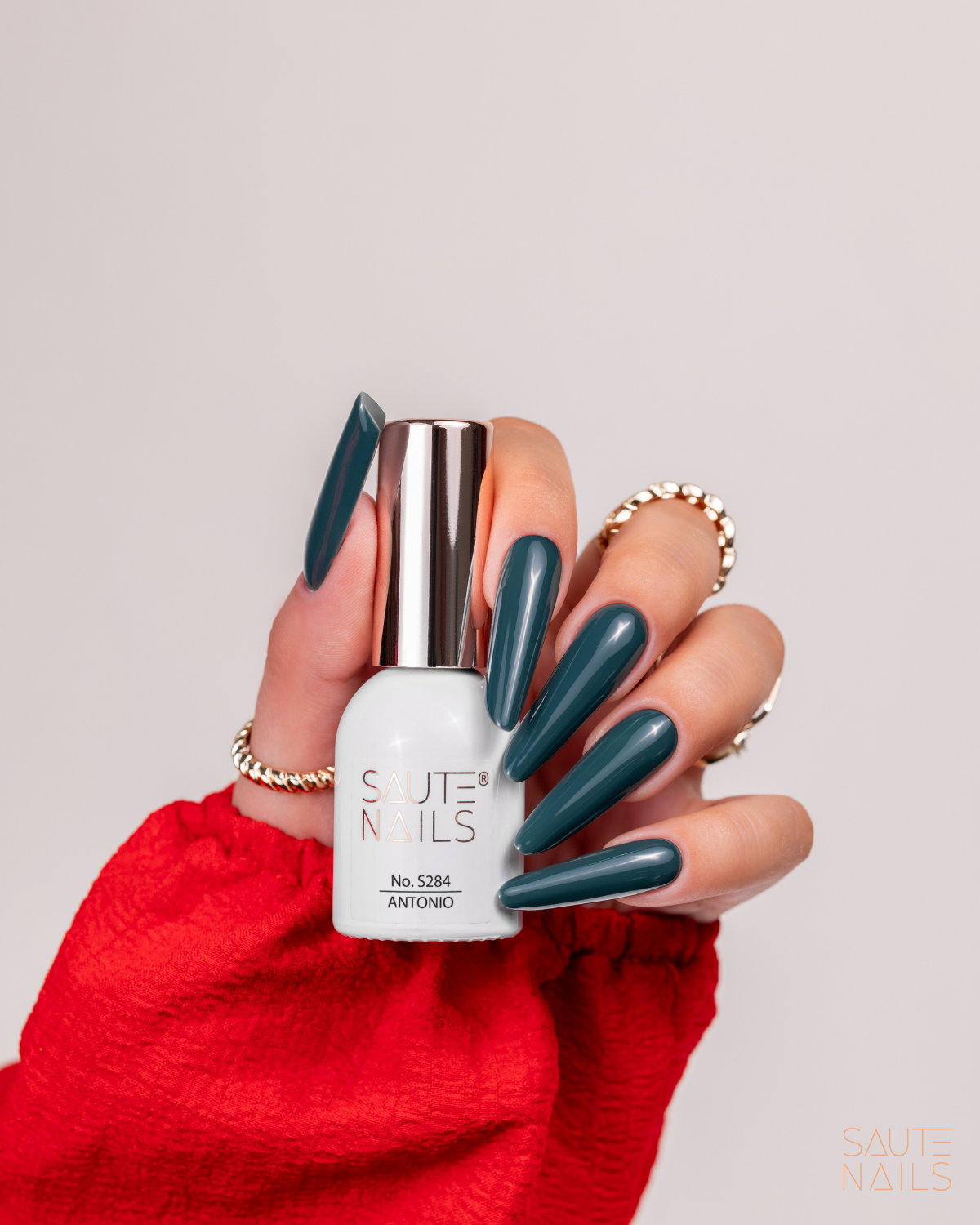 Verniz Gel S284 - Antonio (Verde Escuro) Mão com unhas azuis escuras segurando frasco branco de verniz SAUTE NAILS número 5284