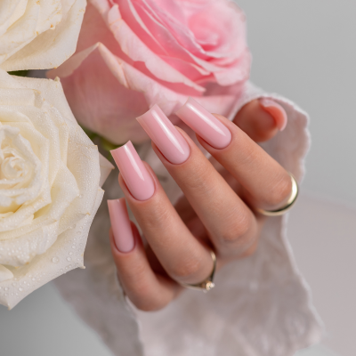 Mão com unhas artificiais rosa claro segurando duas rosas com texto SAUTE NAILS