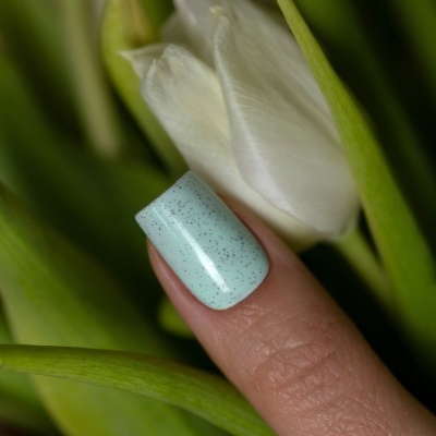 Unha com verniz azul claro e manchas pretas junto a uma flor branca com folhas verdes