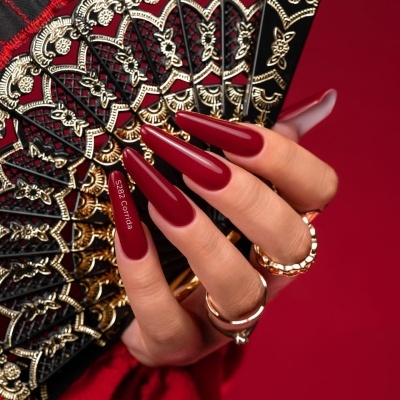 Mão feminina segurando leque preto e dourado com unhas vermelhas longas