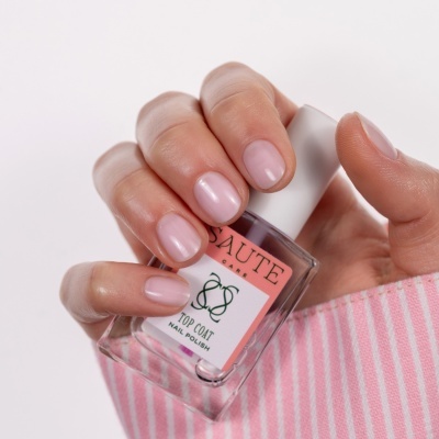 Mão com unhas pintadas segurando frasco de verniz rosa claro