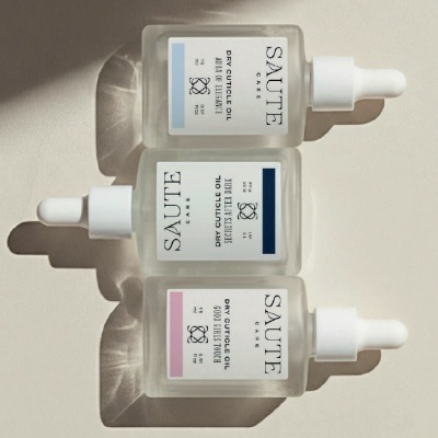 Três frascos de óleo para cutículas SAUTE CARE com conta-gotas sobre fundo cinza claro