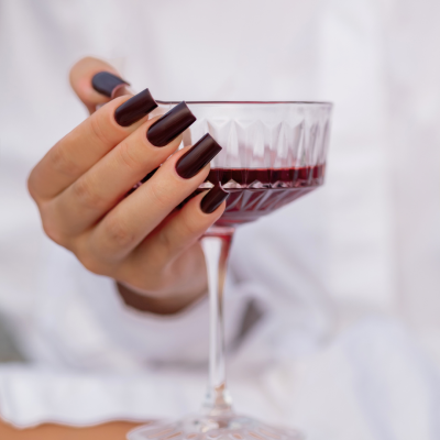 Mão com unhas castanhas escuras segurando taça de vinho tinto